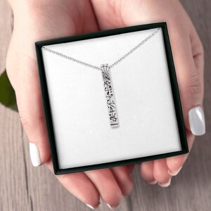 Puede incluir: Un collar con colgante de barra vertical en tono plateado que presenta un delicado diseño de constelación en líneas negras. El colgante cuelga de una fina cadena plateada y se presenta dentro de una caja de regalo negra cuadrada con forro blanco.