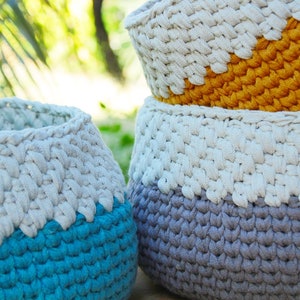 May include: Three crocheted baskets in different colors. The top basket is yellow and white, the middle basket is gray and white, and the bottom basket is blue and white.