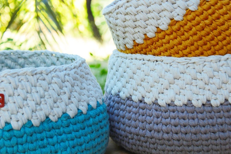 May include: Three crocheted baskets in different colors. The top basket is yellow and white, the middle basket is gray and white, and the bottom basket is blue and white.