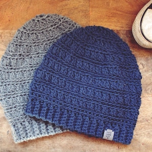 May include: Two crocheted beanies, one grey and one blue, with a small tag that reads "hand made with love".