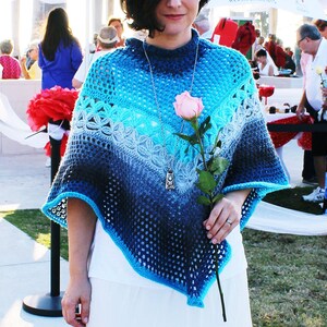 May include: A woman wearing a blue and turquoise crocheted shawl with a silver necklace and a pink rose.