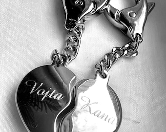 May include: Two silver keychains with a split heart design. The hearts are engraved with the names "Vojta" and "Kiana".