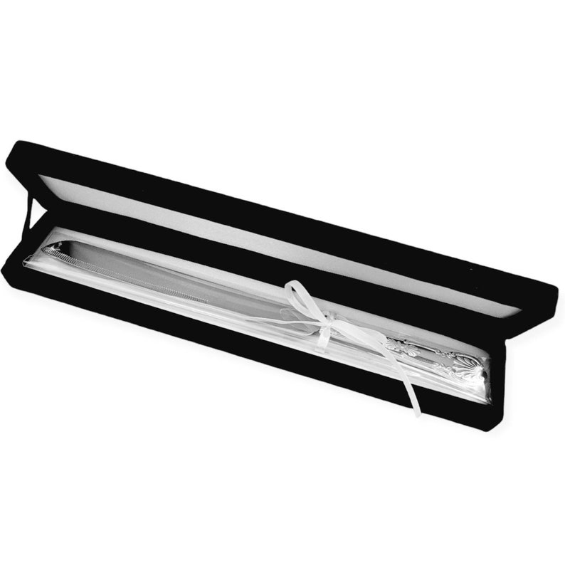 May include: A silver cake knife with an ornate handle is displayed in a black velvet box with a white satin ribbon.