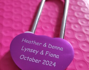 May include: Purple heart-shaped padlock with a silver shackle. The padlock is engraved with the names "Heather & Donna", "Lynsey & Fiona", and the date "October 2024".