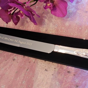 May include: Silver cake knife with a black velvet box. The knife is engraved with "Mr & Mrs Cross 3rd August 2021".