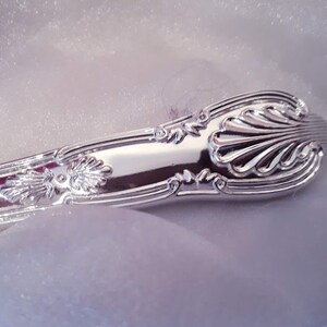 May include: Close-up of the ornate, silver handle of a utensil. The handle has a detailed, floral design.