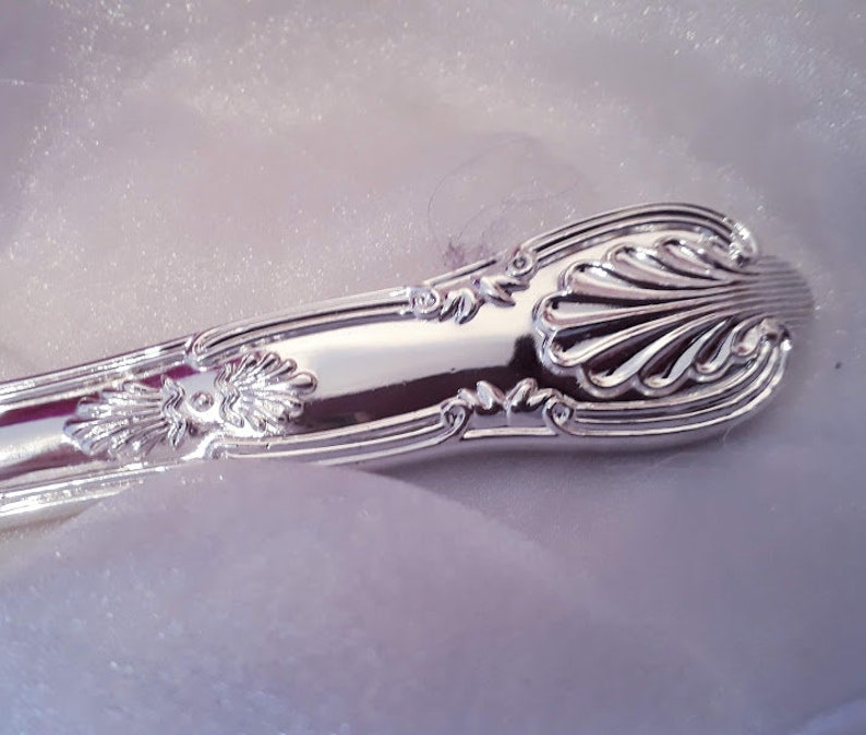 May include: Close-up of the ornate, silver handle of a utensil. The handle has a detailed, floral design.