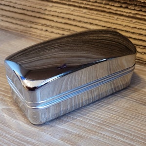 May include: A silver metal rectangular box with a smooth, shiny surface and two raised lines around the perimeter.