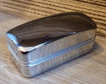 May include: A silver metal rectangular box with a smooth, shiny surface and two raised lines around the perimeter.