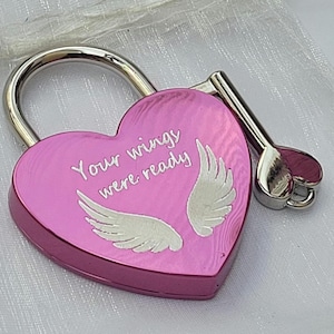 May include: A heart-shaped pink padlock with a silver shackle and a matching silver key. The front of the padlock features the engraved text Your wings were ready, accompanied by a graphic illustration of two white angel wings.