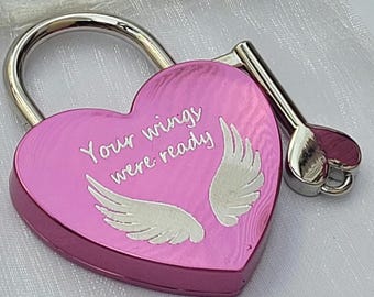 May include: A heart-shaped pink padlock with a silver shackle and a matching silver key. The front of the padlock features the engraved text Your wings were ready, accompanied by a graphic illustration of two white angel wings.