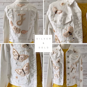 Può includere: Giacca di jeans bianca con decorazioni in argento e oro, tra cui farfalle, api e fiori. La giacca ha una lettera "J" sul retro.