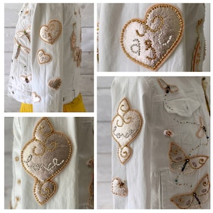 May include: White denim jacket featuring embroidered hearts, butterflies and dragonflies. The hearts are embellished with gold and white beading and the word "Love" is embroidered on them.