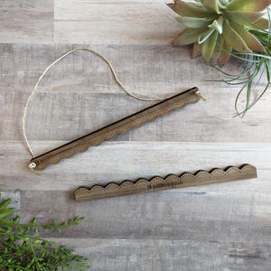 May include: Two wooden wall hanging frames with a scalloped edge design. One frame is suspended by a natural twine string. The other frame has the text "ik prints & fonts" etched into the wood. The frames are a warm brown color.