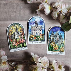 Puede incluir: Tres pegatinas arqueadas con ilustraciones de estilo vidriera de edificios religiosos. La pegatina de la izquierda muestra Kirtland, Ohio con un sol. La del centro muestra Nauvoo, Illinois. La de la derecha muestra Salt Lake City, Utah.