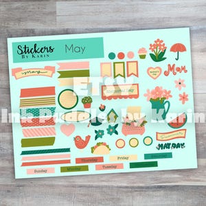 May include: A sheet of stickers with a light blue background. The stickers include banners, washi tape, hearts, flowers, and labels with text like "May," "Mom," and "Summer." The stickers are in shades of pink, green, and orange.