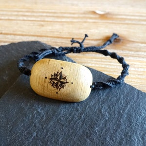 Peut inclure: Un bracelet en bois avec un cordon noir et un motif d'étoile. L'étoile est sculptée dans le bois et a une couleur brun foncé.