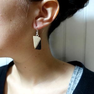 Può includere: Un paio di orecchini in legno con un design geometrico in bianco e nero. Gli orecchini sono appesi a ganci argentati.