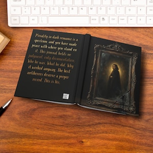 May include: Open journal with a black cover and gold text. The text reads "Morality in dark romance is a spectrum..." The right page features a framed portrait of a person in dark clothing. A keyboard is visible in the background.