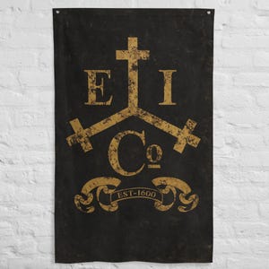 Könnte beinhalten: Schwarze Wandfahne mit einem goldenen Emblem mit den Buchstaben "E", "I" und "C" mit Kreuzsymbolen. Der Text "EST-1600" wird auf einem Banner unter dem Emblem angezeigt. Die Fahne hat ein verwittertes, Vintage-Aussehen.