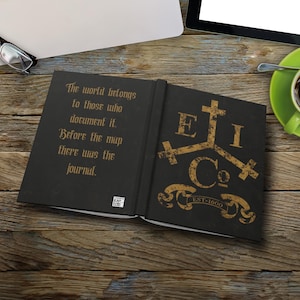 May include: Open black journal with gold lettering and a decorative emblem. The text reads "The world belongs to those who document it. Before the map there was the journal." The journal also has the text "EI Co. EST-1600".
