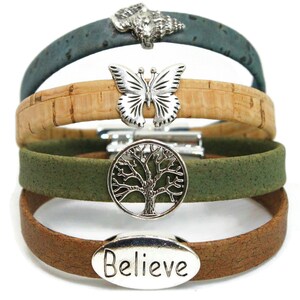 May include: Four cork bracelets in shades of green, brown, and tan. Each bracelet features a silver charm: a wolf, a butterfly, a tree of life, and the word "Believe". The bracelets are stacked on top of each other.