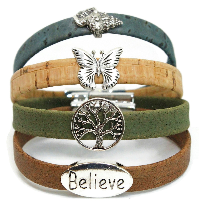May include: Four cork bracelets in shades of green, brown, and tan. Each bracelet features a silver charm: a wolf, a butterfly, a tree of life, and the word "Believe". The bracelets are stacked on top of each other.