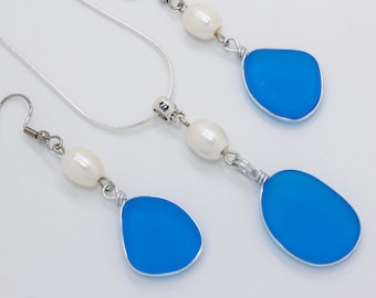 May include: A jewelry set featuring a necklace and earrings. The set includes a silver chain necklace and silver wire wrapped earrings and pendant. Each piece has a bright blue, irregular shaped stone and a white pearl.