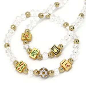May include: A beaded necklace featuring clear faceted crystal beads, polished gold-tone spherical beads, and rectangular gold-tone mahjong tiles with green, red, and black symbols. A single white spherical bead with a gold star pattern is included.