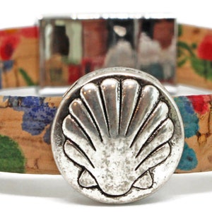 May include: A cork bracelet with a floral pattern in red, blue, yellow, and green. The bracelet has a silver-colored clasp and a large, round, silver-colored seashell-shaped button as a focal point. The bracelet is approximately 0.75 inches wide.
