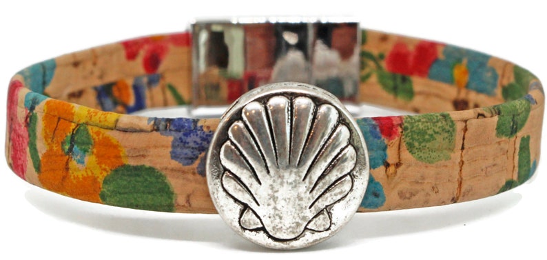 May include: A cork bracelet with a floral pattern in red, blue, yellow, and green. The bracelet has a silver-colored clasp and a large, round, silver-colored seashell-shaped button as a focal point. The bracelet is approximately 0.75 inches wide.