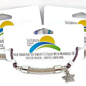 Pode incluir: Tr&ecirc;s pulseiras com um tubo transparente cheio de areia, conectadas por metal prateado. Cada pulseira tem um cord&atilde;o de cor diferente: azul, roxo e azul-petr&oacute;leo. Um berloque de estrela do mar pende de cada pulseira. A embalagem diz "Sea Ranch Handmade Jewelry".