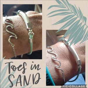Pode incluir: Duas pulseiras s&atilde;o mostradas. Uma &eacute; um design de onda prateada com uma corrente. A outra &eacute; uma pulseira de couro verde claro com detalhes prateados. O texto "Toes in SAND" est&aacute; na parte inferior da imagem.