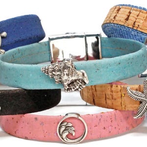 May include: A collection of nautical-themed bracelets in various colors, including blue, black, and pink. Each bracelet features a unique charm, such as a seashell, starfish, or anchor. The bracelets are made of cork and other materials.