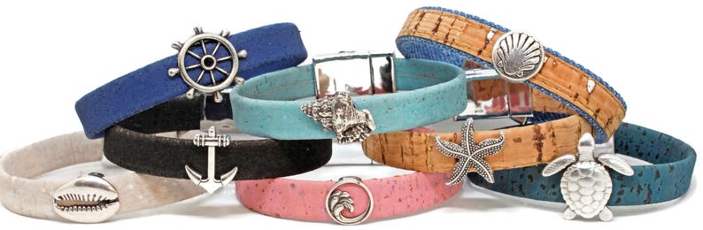 May include: A collection of nautical-themed bracelets in various colors, including blue, black, and pink. Each bracelet features a unique charm, such as a seashell, starfish, or anchor. The bracelets are made of cork and other materials.
