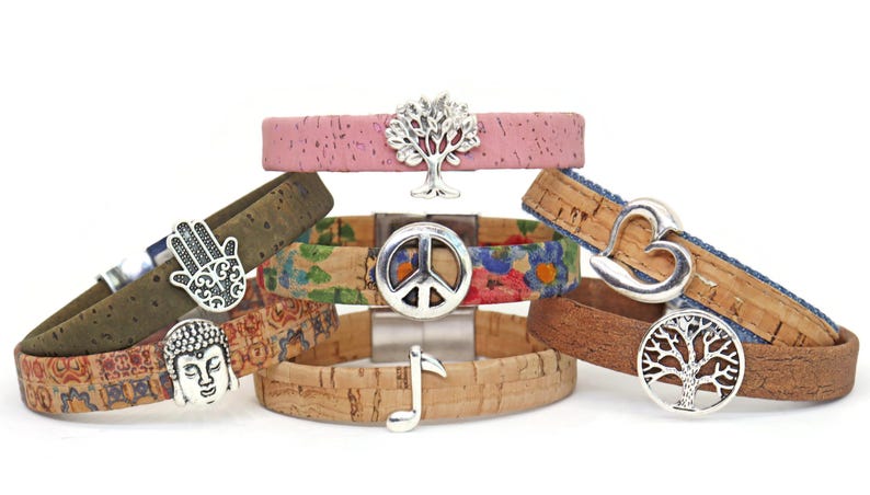 May include: A collection of cork bracelets with various designs and silver-tone charms. The bracelets feature different patterns and colors, including floral, pink, and natural cork. Charms include a tree, peace sign, hand, heart, and musical note.