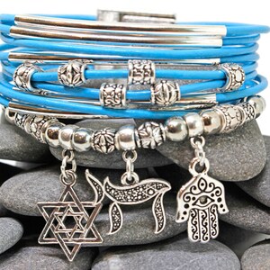 May include: A multi-strand bracelet with light blue leather cords and silver-toned metal accents. The bracelet features decorative beads and charms, including a Star of David, a Chai symbol, and a Hamsa hand.