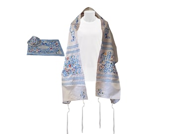 May include: A white and silver tallit with blue embroidered floral designs, displayed on a mannequin. A matching kippah and prayer mat with similar embroidery are also present. The tallit has long tassels.