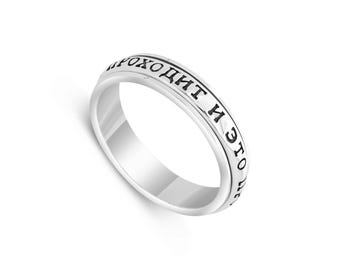 May include: A silver ring with the inscription "И это пройдет" in black Cyrillic script. The ring has a smooth, polished surface and a rotating band. The ring is set against a white background.