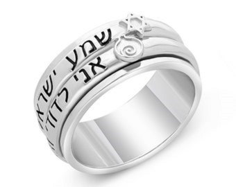 May include: A silver ring with Hebrew text and a Star of David charm. The ring has a spinning band with engraved lettering. The design includes a small, decorative spiral element. The ring is highly polished and reflects light.