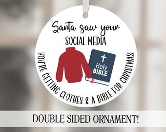 Może przedstawiać: Okrągła biała ozdoba choinkowa z tekstem "Santa saw your social media you're getting clothes & a bible for Christmas" oraz czerwonym swetrem i książką z krzyżem i tekstem "Holy Bible" na niej.