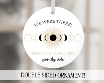 May include: White round ornament with a black and gold solar eclipse design. The text "WE WERE THERE!" is at the top and "SOLAR ECLIPSE 04.08.2024" is below the design. The text "your city, state" is below the date. The text "DOUBLE SIDED ORNAMENT!" is at the bottom and "carolinamade" is below that.