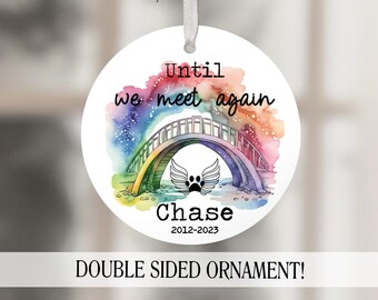 May include: A white round ornament with a rainbow bridge and paw print wings. The text reads "Until we meet again" and "Chase 2012-2023".  Double sided ornament.