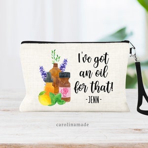 May include: A white canvas zippered pouch with a black zipper and a black strap. The pouch has a watercolor illustration of essential oil bottles and the text "I've got an oil for that! - JENN -" printed on it.