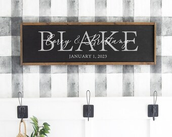 May include: A black wooden sign with white text that reads "Corey & Brittany, January 1, 2023". The sign is hanging on a wall with a black and white checkered pattern.