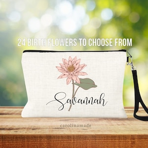 May include: A white canvas makeup bag with a black zipper and a black strap. The bag features a pink flower illustration and the name "Savannah" written in cursive. The text "carolinmade" is printed in the bottom corner.