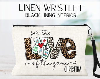 May include: A white linen wristlet with a black lining. The wristlet features a leopard print design with the word "LOVE" spelled out in large letters. The letters are decorated with mahjong tiles and the text "for the love of the game Christina".