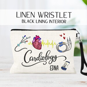 May include: A beige linen wristlet with a black wrist strap and black interior lining. The front features a colorful illustration of a human heart, medical tubing, a yellow EKG line, three red hearts, and a medical device, with the text Cardiology and EDNA.