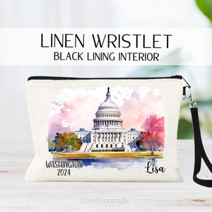 May include: Linen wristlet with a black lining interior. The wristlet features a watercolor painting of the U.S. Capitol building with the text "Washington 2024" and the name "Lisa". It has a black wrist strap.