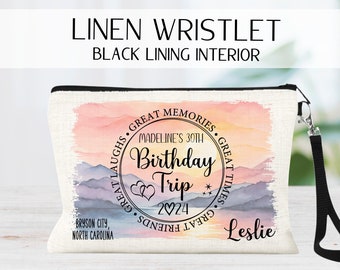 May include: A white linen wristlet with a black zipper and a black wrist strap. The front of the wristlet features a watercolor-style mountain scene with a circle containing the text "Madeline's 30th Birthday Trip 2024" and the words "Great Laughs, Great Memories, Great Times, Great Friends". The text "Bryson City, North Carolina" and "Leslie" are also printed on the wristlet.
